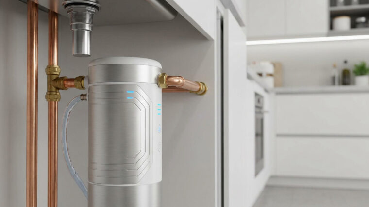 Adoucisseur d'eau compact en acier brossé installé sous un évier de cuisine avec des raccordements en cuivre.