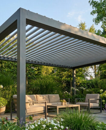 Une pergola bioclimatique en aluminium gris installée sur une terrasse entourée de plantes luxuriantes et d'un salon de jardin.