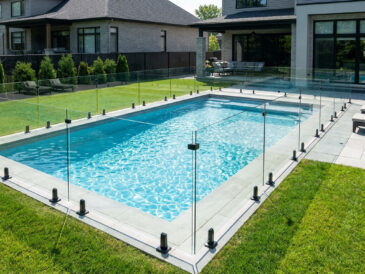 Clôture de piscine en verre trempé minimaliste entourant une piscine creusée dans un jardin résidentiel moderne.