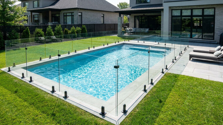 Clôture de piscine en verre trempé minimaliste entourant une piscine creusée dans un jardin résidentiel moderne.