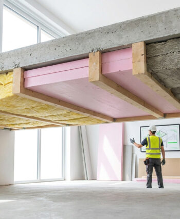 Ouvrier inspectant l'isolation d'un plafond avec différents matériaux comme la laine de verre et des panneaux isolants.