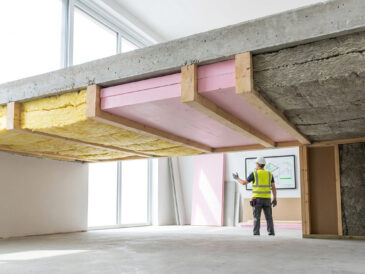 Ouvrier inspectant l'isolation d'un plafond avec différents matériaux comme la laine de verre et des panneaux isolants.