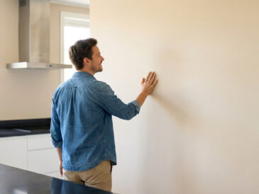 Un homme en chemise en jean touche un mur fraîchement peint de couleur beige dans une cuisine moderne.
