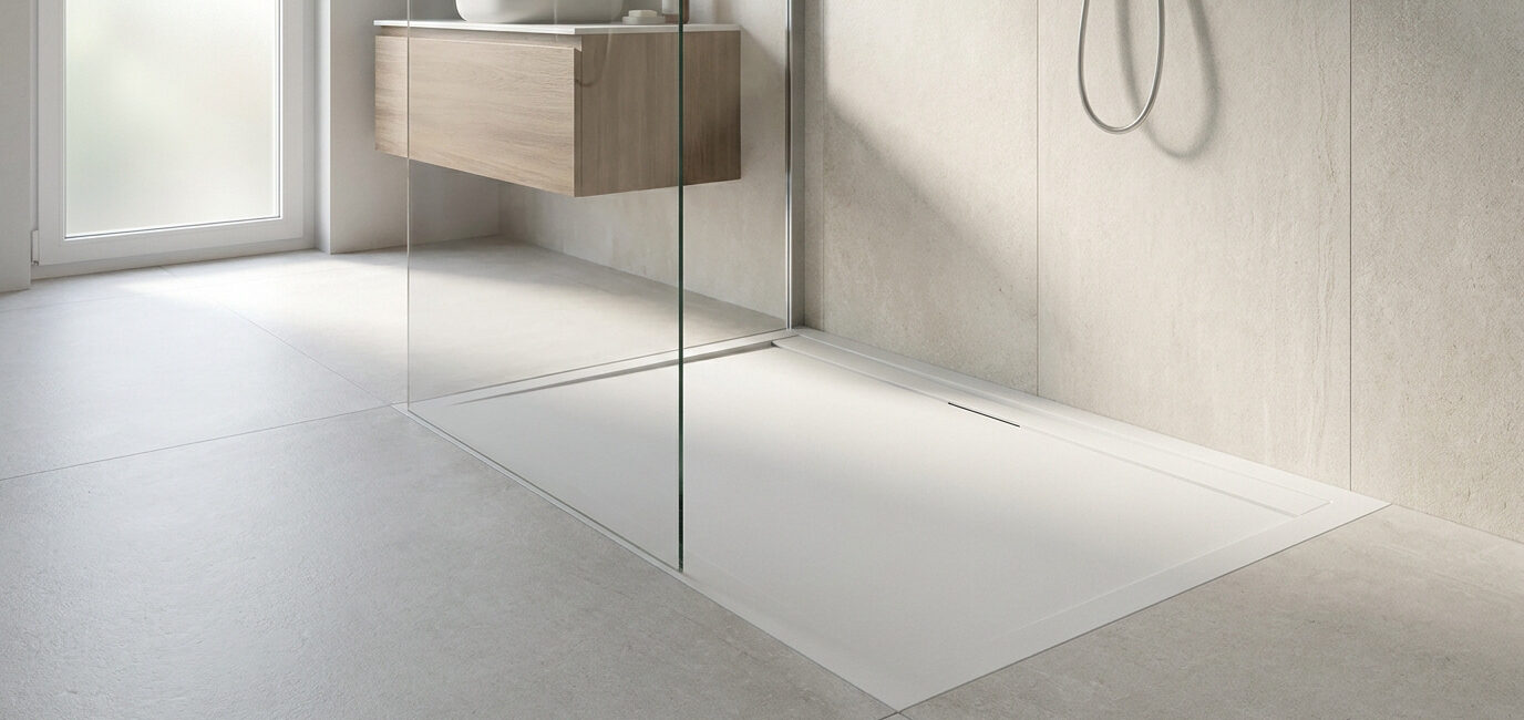 Receveur de douche blanc extra plat dans une salle de bain moderne avec paroi en verre et meuble vasque en bois.