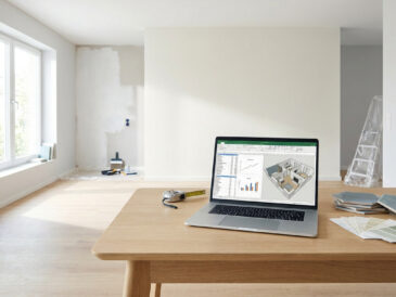 Un ordinateur portable sur une table en bois affichant un plan 3D et un budget dans un appartement en cours de rénovation.