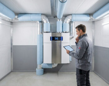 Un technicien vérifie l'installation d'une VMC double flux connectée avec une tablette dans un local technique.